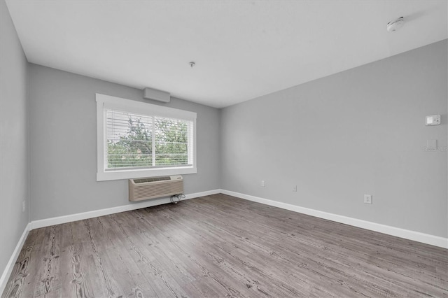 unfurnished room featuring baseboards, a wall mounted AC, and wood finished floors