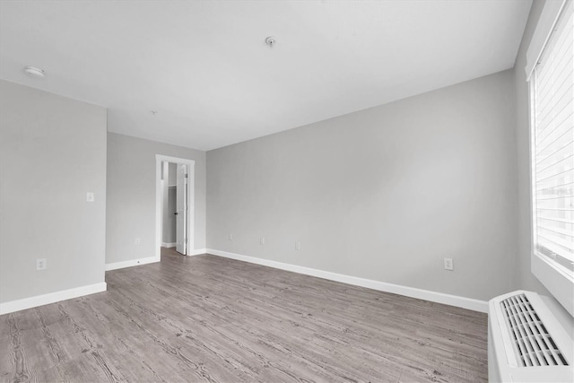 unfurnished room featuring an AC wall unit, baseboards, and wood finished floors