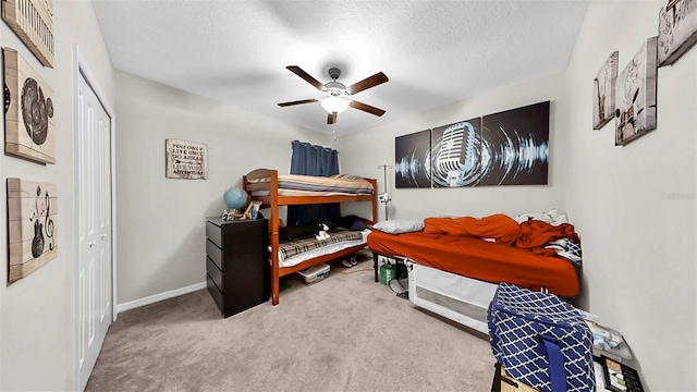 bedroom with a textured ceiling, baseboards, a ceiling fan, a closet, and carpet floors