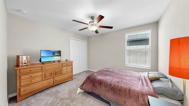 bedroom featuring light colored carpet, baseboards, a ceiling fan, and a closet