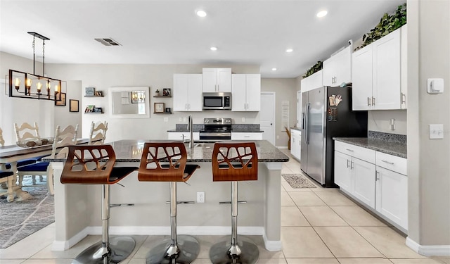 kitchen featuring white cabinets, appliances with stainless steel finishes, a kitchen breakfast bar, and a kitchen island with sink