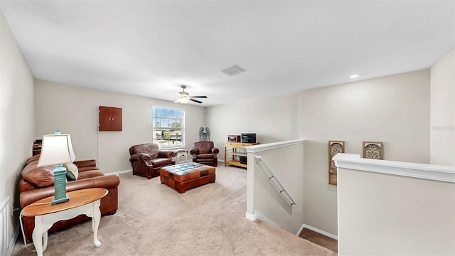 living room featuring ceiling fan, visible vents, baseboards, and light carpet