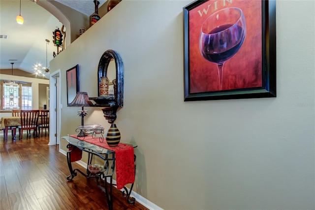 hallway featuring baseboards, vaulted ceiling, visible vents, and wood finished floors