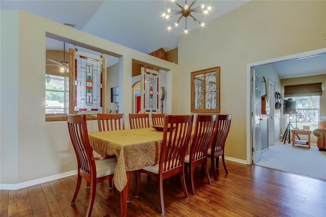 dining space featuring baseboards, a towering ceiling, wood finished floors, and ceiling fan with notable chandelier