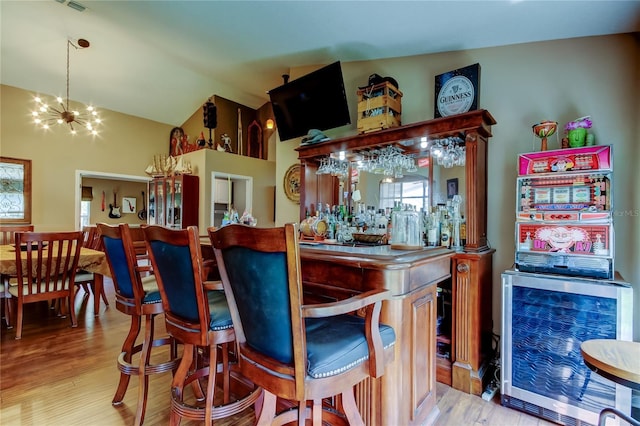 bar with a bar, light wood-style flooring, vaulted ceiling, and a notable chandelier