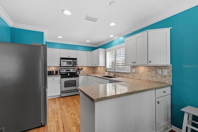 kitchen with a sink, white cabinetry, appliances with stainless steel finishes, a peninsula, and visible vents