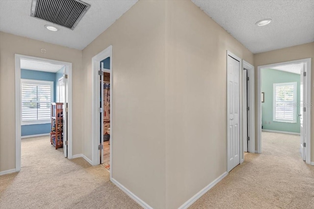 hall featuring light carpet, baseboards, visible vents, and a textured ceiling