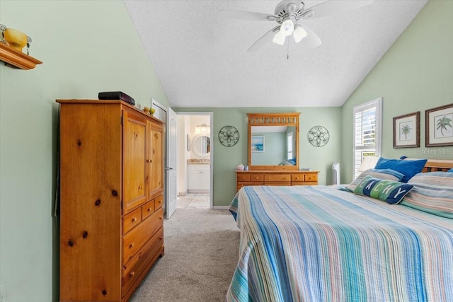 bedroom with light colored carpet, vaulted ceiling, a textured ceiling, ceiling fan, and ensuite bathroom