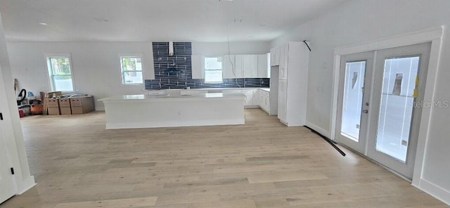745 31st Ave N, Saint Petersburg, FL 33704 - kitchen featuring a center island, white cabinets, french doors, light wood-type flooring, and decorative backsplash