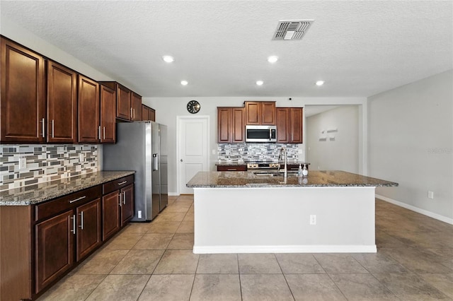 14050 Arbor Pines Dr, Riverview, FL 33579 - kitchen featuring stainless steel appliances, decorative backsplash, dark stone countertops, an island with sink, and light tile patterned flooring