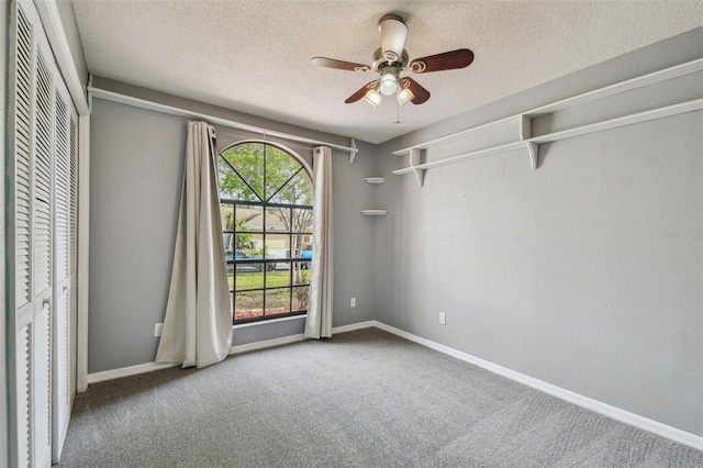 carpeted empty room with a textured ceiling, baseboards, and a ceiling fan