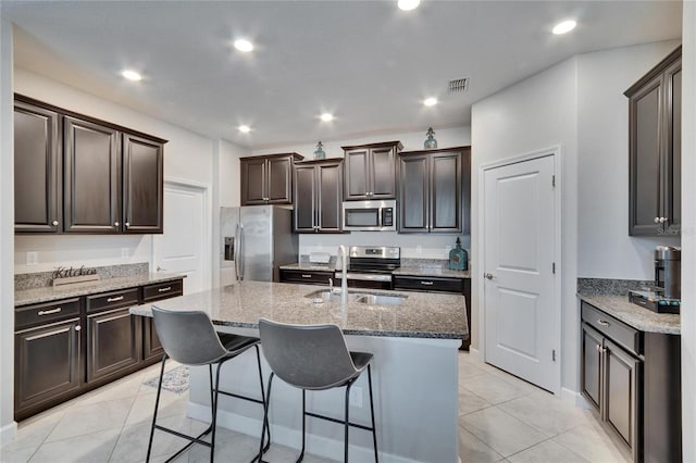 kitchen featuring an island with sink, light stone counters, a breakfast bar, stainless steel appliances, and a sink