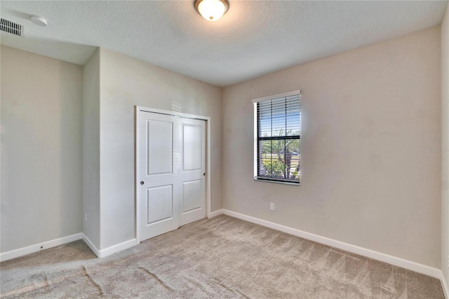 unfurnished bedroom with a textured ceiling, visible vents, baseboards, and carpet floors