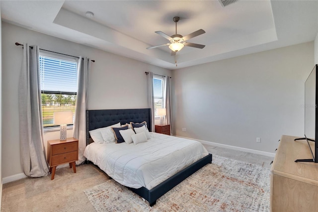 bedroom featuring visible vents, baseboards, light carpet, and a tray ceiling
