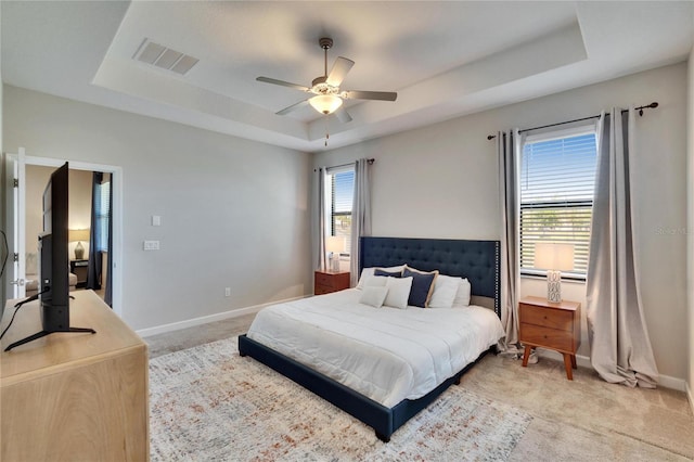 bedroom with a raised ceiling, baseboards, visible vents, and light carpet