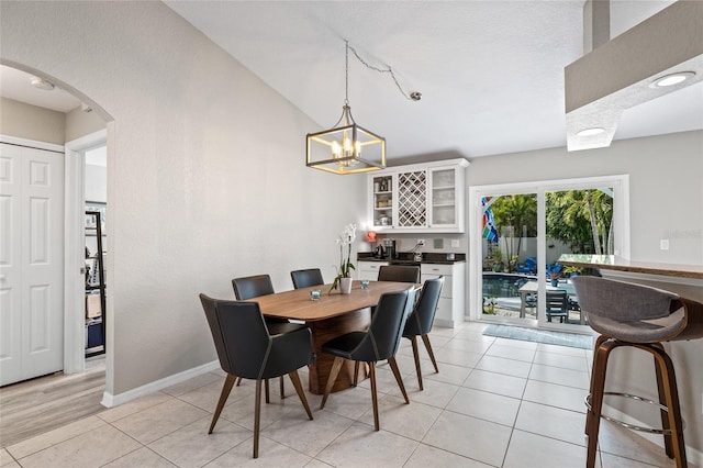 dining area featuring bar area, arched walkways, baseboards, a notable chandelier, and light tile patterned flooring