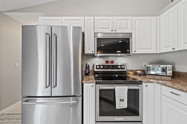 kitchen featuring a toaster, dark stone countertops, white cabinetry, and stainless steel appliances