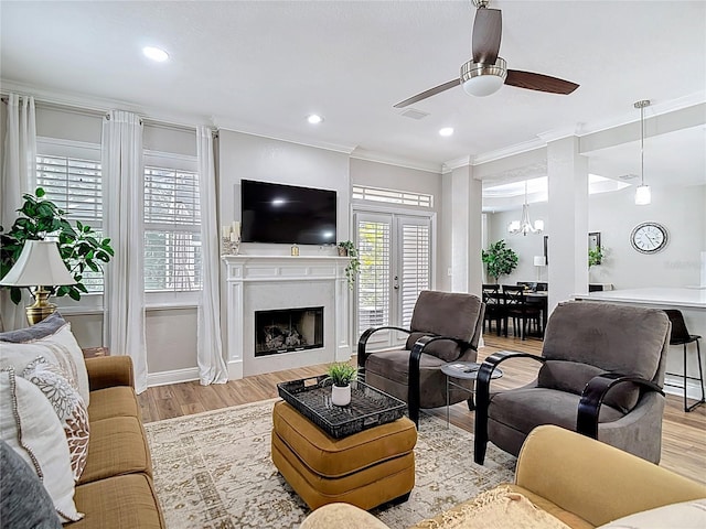 living area with recessed lighting, a fireplace, crown molding, wood finished floors, and ceiling fan with notable chandelier