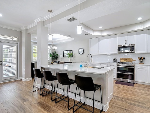 kitchen with a sink, appliances with stainless steel finishes, visible vents, light countertops, and ornamental molding