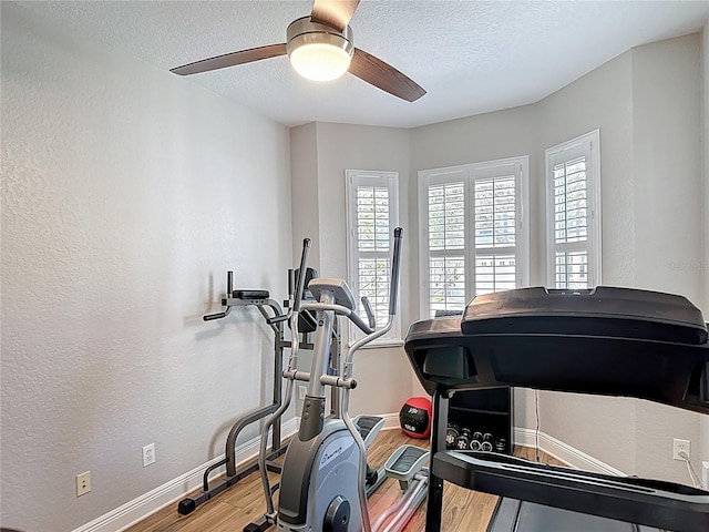 exercise room with a textured ceiling, ceiling fan, wood finished floors, and baseboards