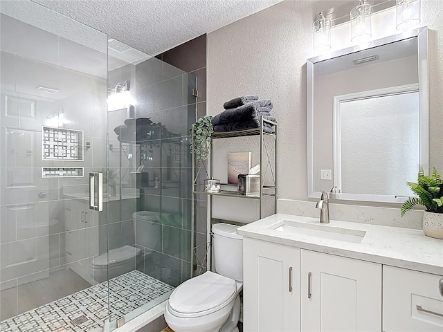 bathroom with vanity, toilet, a stall shower, a textured wall, and a textured ceiling
