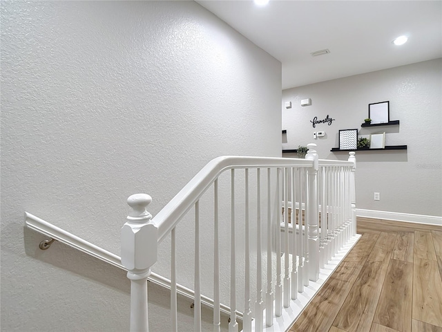 stairway with recessed lighting, a textured wall, wood finished floors, and baseboards