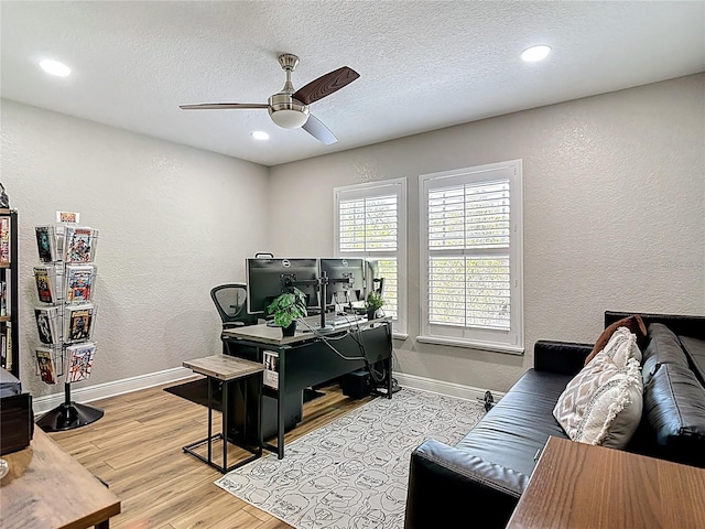 office area with wood finished floors, a textured wall, a ceiling fan, and baseboards