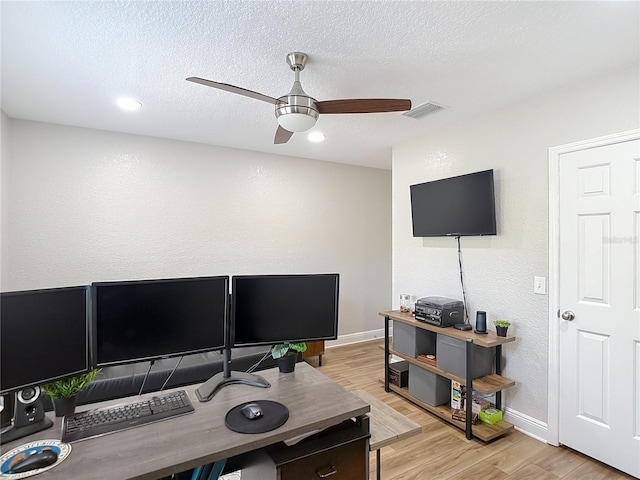home office with light wood-style flooring, a textured wall, baseboards, visible vents, and a ceiling fan