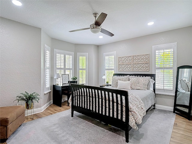bedroom featuring multiple windows, a textured wall, and wood finished floors