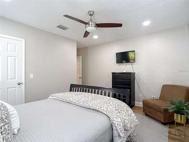 bedroom with recessed lighting, wood finished floors, a textured wall, visible vents, and a ceiling fan