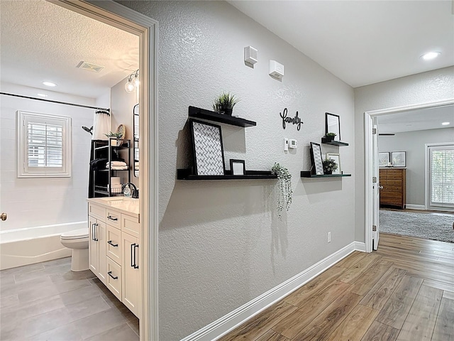 corridor with recessed lighting, wood finished floors, a textured wall, baseboards, and visible vents