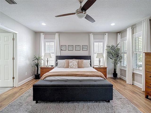 bedroom with light wood finished floors, visible vents, multiple windows, and baseboards