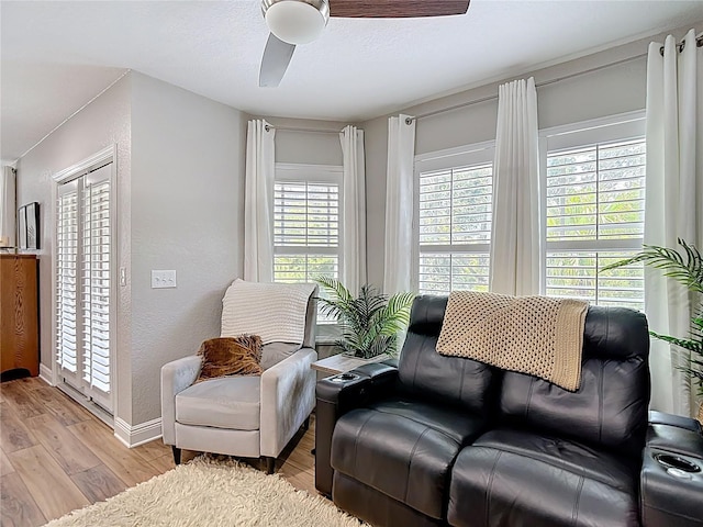 living area featuring ceiling fan, a textured wall, light wood-style flooring, and baseboards