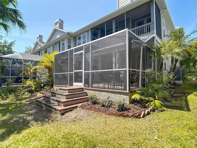 rear view of property featuring a chimney, a balcony, central AC unit, and a lawn