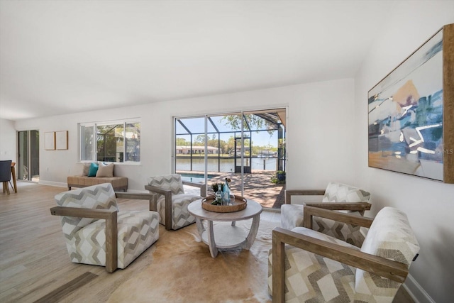 living room with baseboards, a sunroom, light wood-style flooring, and a healthy amount of sunlight