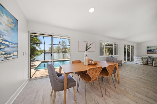 dining room featuring baseboards, a water view, a wealth of natural light, and light wood-type flooring