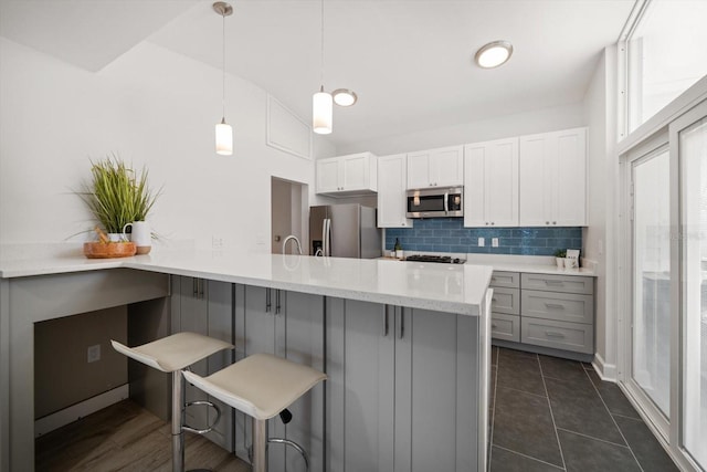 kitchen featuring a kitchen breakfast bar, appliances with stainless steel finishes, a peninsula, hanging light fixtures, and decorative backsplash