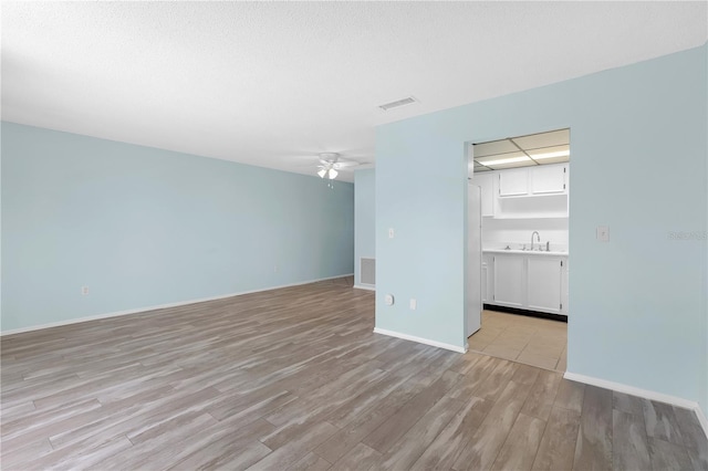 unfurnished living room with visible vents, a ceiling fan, light wood-style flooring, and a sink