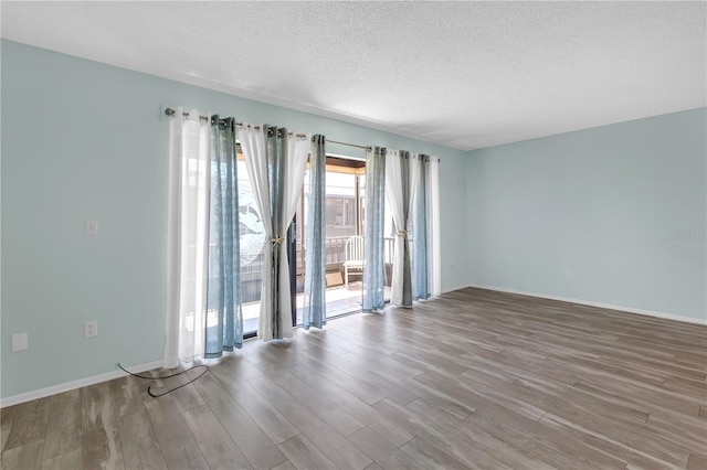 unfurnished room featuring a textured ceiling, wood finished floors, and baseboards