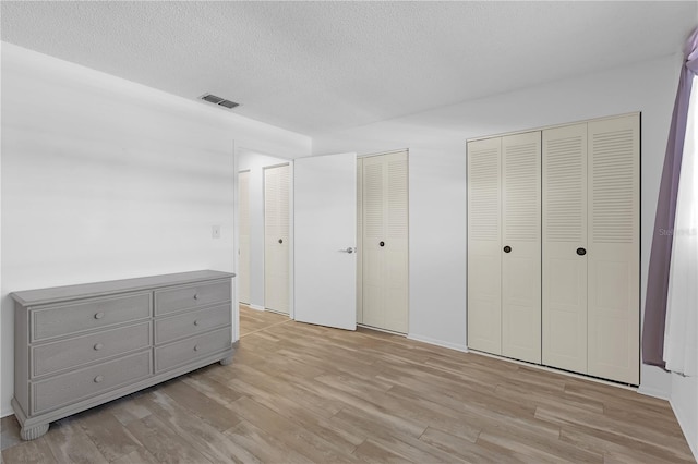 unfurnished bedroom featuring a textured ceiling, two closets, light wood-style flooring, and visible vents