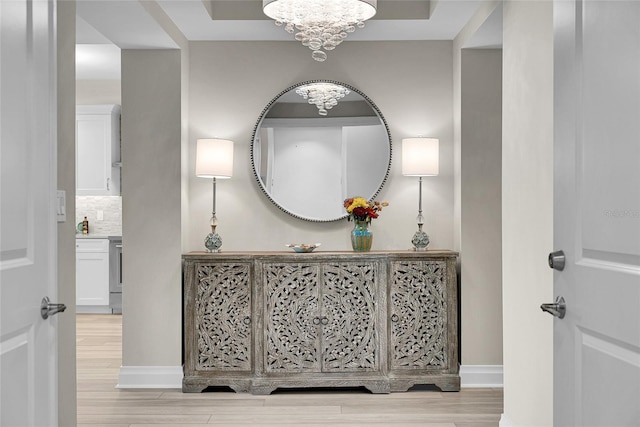 corridor featuring baseboards, wood finished floors, and an inviting chandelier