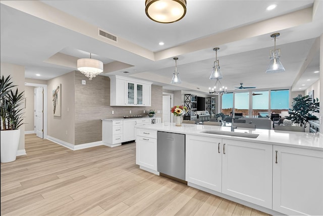 kitchen with a tray ceiling, visible vents, stainless steel dishwasher, a sink, and light wood-style floors