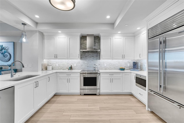 kitchen with white cabinets, stainless steel appliances, a sink, light wood-style floors, and wall chimney range hood
