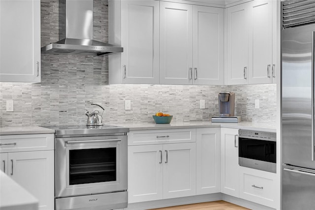 kitchen featuring wall chimney range hood, decorative backsplash, white cabinetry, and stainless steel appliances