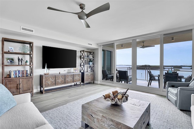 living area with wood finished floors, expansive windows, ceiling fan, baseboards, and visible vents