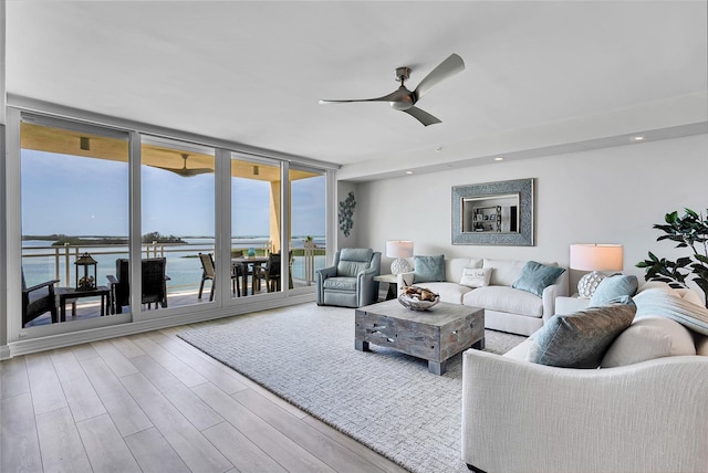 living area featuring a ceiling fan, wood finished floors, a water view, a wall of windows, and recessed lighting