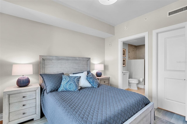 bedroom with ensuite bath, wood finished floors, visible vents, and baseboards
