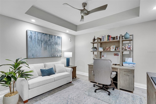office space featuring baseboards, recessed lighting, light wood-style floors, a ceiling fan, and a raised ceiling