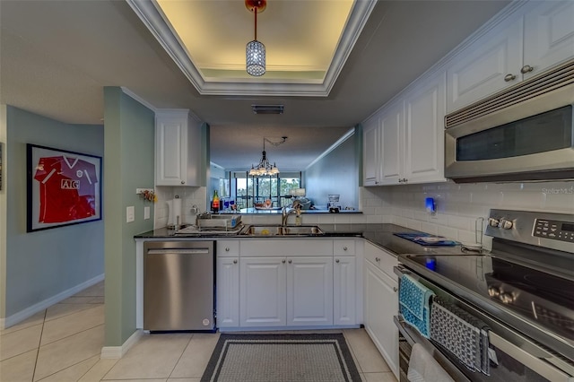kitchen featuring ornamental molding, a raised ceiling, dark countertops, white cabinets, and appliances with stainless steel finishes