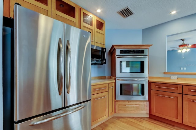 kitchen featuring light countertops, appliances with stainless steel finishes, glass insert cabinets, light wood-style flooring, and visible vents